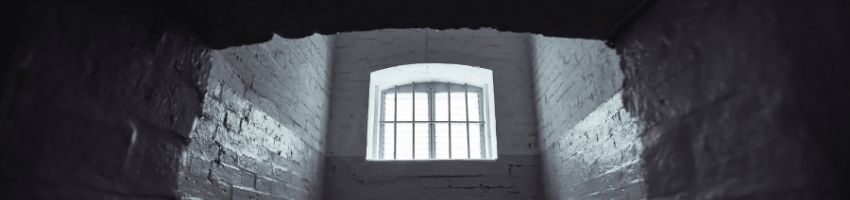 A window of an abandoned prison with lights shing through.
