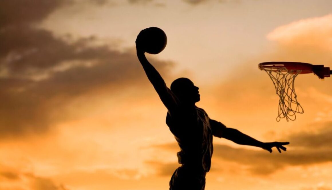 A silhouette of a man playing basketball in twilight.
