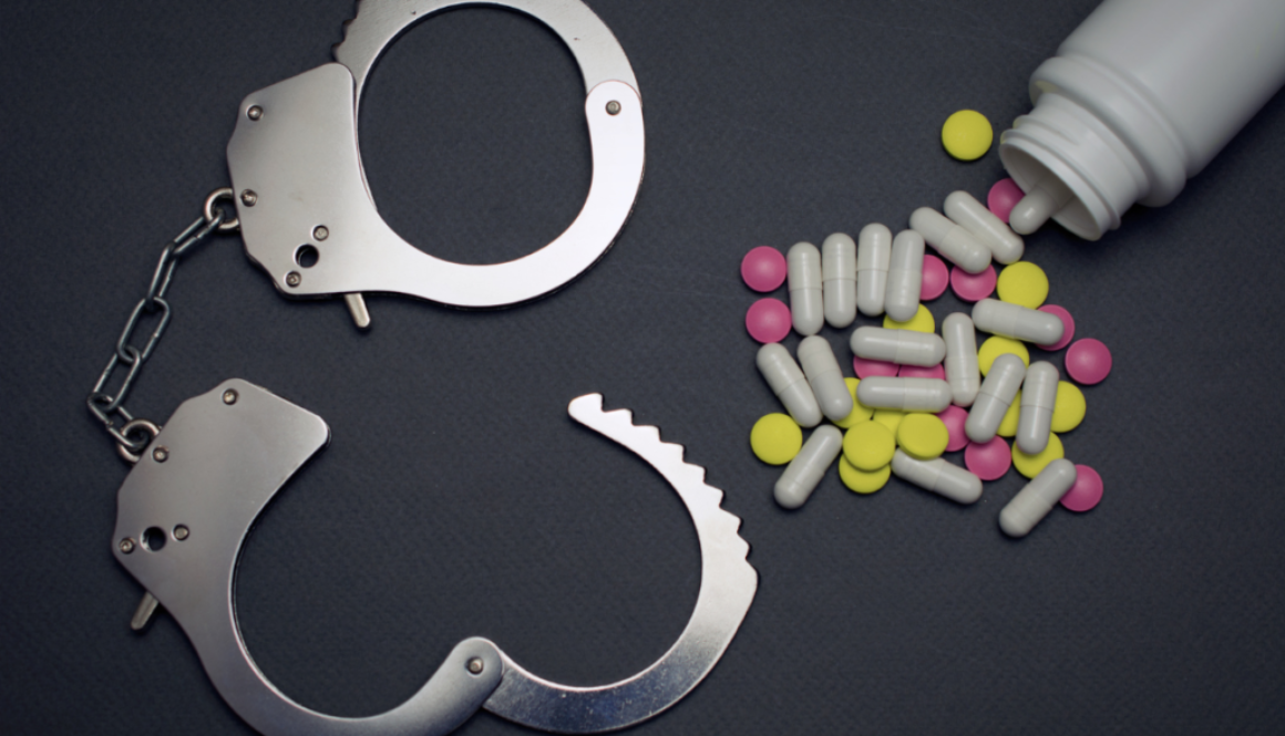 Colorful pills scattered beside an unlocked handcuff.