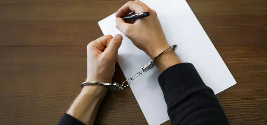 A person who committed the most common felonies have his hands handcuffed while writing in a piece of paper